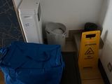 a blue bag sitting on the floor next to a trash can and a yellow caution sign