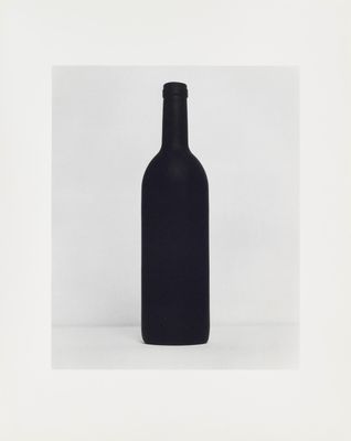 a black bottle of wine sitting on top of a white table