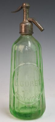 une bouteille en verre vert munie d'une poignée en laiton, posée sur une surface blanche