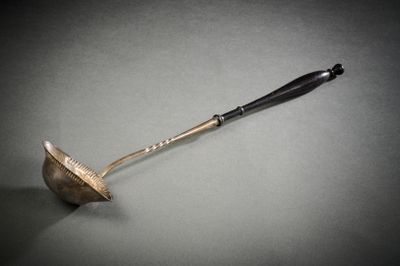 une vieille cuillère en métal avec un manche en bois posée sur une surface grise