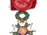 Gros plan sur une médaille sur fond blanc, accompagnée d'un ruban rouge