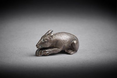 une vieille figurine en argent représentant une souris posée sur une surface grise