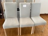 quatre chaises blanches, avec une étiquette de prix, posées sur un plancher en bois