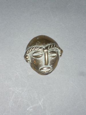 l'image d'un petit masque en bronze sur un fond blanc