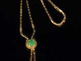a gold necklace with a green stone pendant on a black background