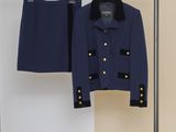 un tailleur-jupe bleu marine et une veste suspendus à un cintre devant un mur beige