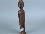 une vieille statue en bois représentant une personne, avec une étiquette accrochée à son cou