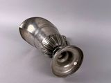 a silver vase that is sitting on a white surface