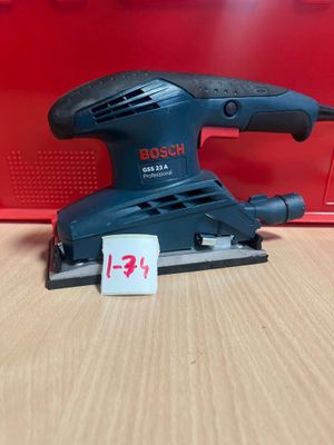 une ponceuse orbitale Bosch posée sur une table, à côté d'une boîte rouge