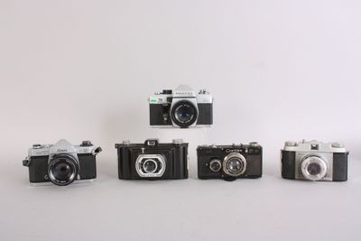 four old cameras are lined up on a white surface