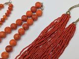 two pieces of red beads and a tassel on a white surface