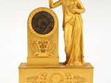 une image représentant une horloge en or surmontée d'une statue de femme