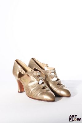 une paire de chaussures dorées posées sur une surface blanche, sur fond blanc