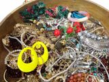 a wooden bowl filled with lots of jewelry and a pair of scissors