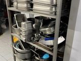 several pots and pans are stacked on a metal shelf in a kitchen