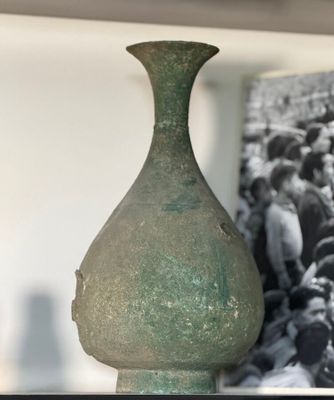 a green vase sitting on a shelf with a picture in the background
