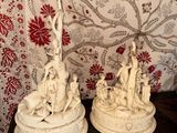 deux statues posées sur une table, avec en arrière-plan un papier peint rouge et blanc