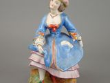 an antique figurine of a woman in a blue dress and hat sitting on a rock