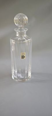 une photo d'une bouteille en verre transparent posée sur une surface blanche