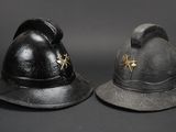pair of antique fireman ' s helmets on display against a black background