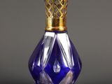 flacon de parfum en verre violet avec un bouchon doré, posé sur une surface grise