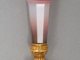 a pink and white vase with a gold base on a table