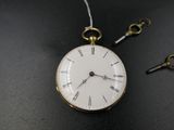 une montre de poche avec une clé posée sur une table