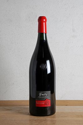 the bottle of red wine is sitting on a wooden table