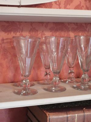 Plusieurs verres à vin vides sont alignés sur une étagère devant un mur recouvert de papier peint.