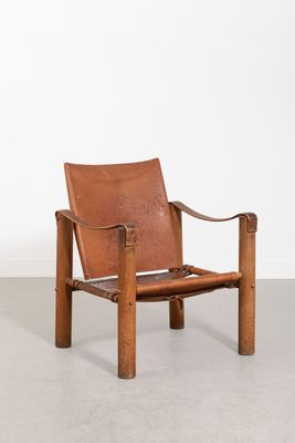 un fauteuil en cuir marron avec une structure en bois et des accoudoirs, adossé à un mur blanc