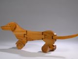 a wooden toy of a dog on wheels on a white surface