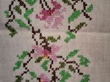 a cross stitched picture of pink flowers on a white table cloth