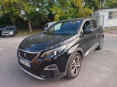 La voiture noire est garée sur le parking, près des arbres.
