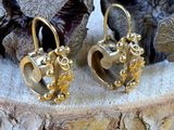 a pair of gold earrings sitting on top of a piece of wood