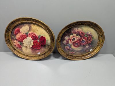 une paire de tableaux anciens représentant des motifs floraux, dans des cadres dorés, posés sur une table blanche