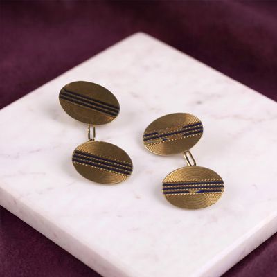 un gros plan sur une paire de boutons de manchette rayés d'or et de bleu posés sur une surface en marbre