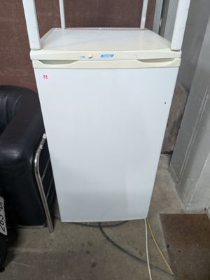 a small white refrigerator sitting next to a black chair