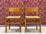 pair of wooden chairs against a wall with a red floral wallpaper