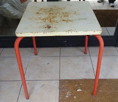 une petite table au plateau rouillé, devant un magasin