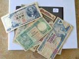 de nombreux billets de banque de différentes valeurs posés sur la table, à côté d'un ordinateur portable