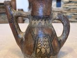 un vase marron posé sur une table, avec un mur en pierre en arrière-plan