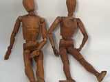 deux mannequins en bois assis l'un à côté de l'autre sur une surface blanche