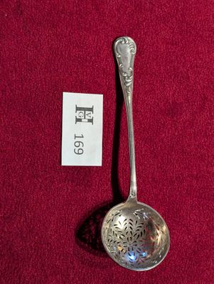 une cuillère en argent posée sur une nappe rouge, avec une étiquette accrochée dessus