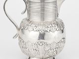 une cruche ancienne en argent, munie d'une anse et ornée d'un motif floral