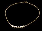 a gold necklace with pearls on a black background