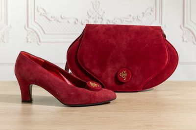 a pair of red sued shoes and a red purse on a table