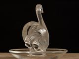 glass swan figurine sitting on a glass plate on a wooden table