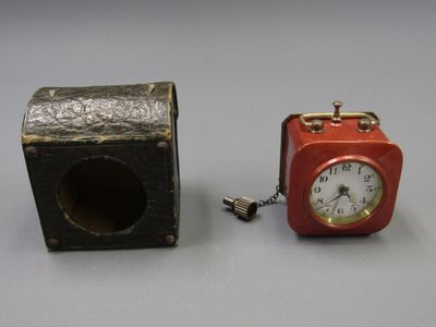 une petite horloge rouge posée à côté d'une petite boîte noire