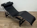 une photo d'une chaise longue en cuir noir posée sur un parquet