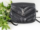 a black saint laurent bag next to a plant on a white surface